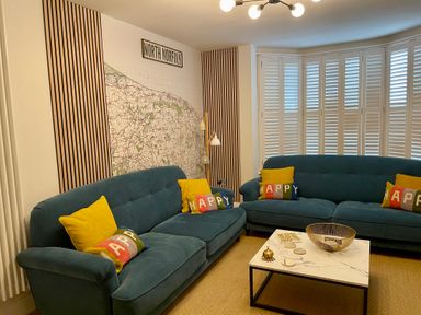 A living room with two blue sofas with colorful and yellow cushions a marble coffee table and a large map on the wall at Happy Place in Sheringham