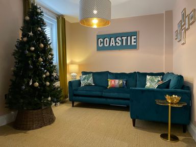 A living room with a decorated Christmas tree blue sofa and a lamp at Happy Place in Sheringham