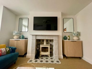 A living room with a mounted television above a fireplace and two cabinets with mirrors and lamps at Happy Place in Sheringham