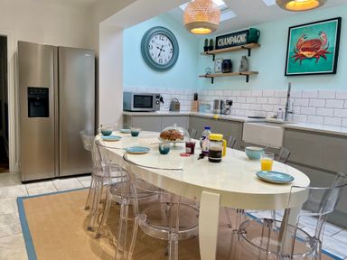 A kitchen with a white oval table set for breakfast clear chairs a stainless steel refrigerator and blue walls at Happy Place in Sheringham