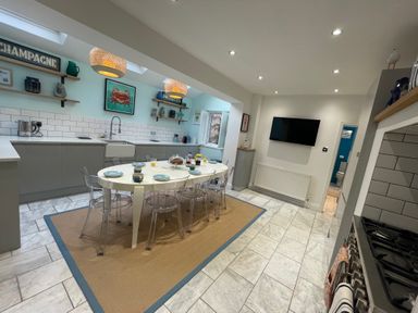 A kitchen with a dining table and chairs a wall mounted television and shelves with decor at Happy Place in Sheringham