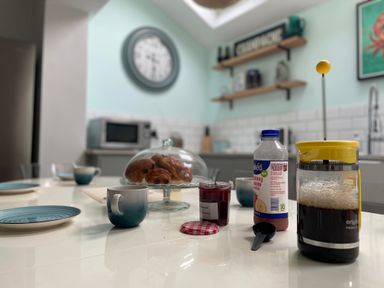 A kitchen table with a French press coffee maker jar of jam cup and plates in a kitchen at Happy Place in Sheringham