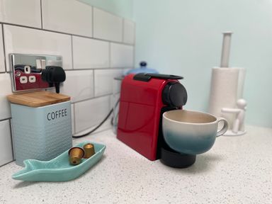 A red coffee machine with a cup on a counter next to a container labeled coffee and coffee capsules at Happy Place in Sheringham