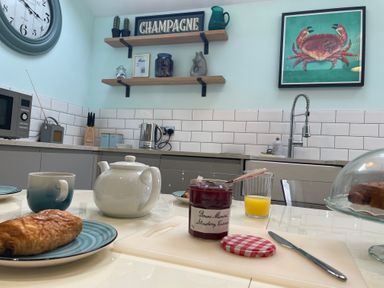 A kitchen with a white teapot cup jar of strawberry jam glass of orange juice and shelves with decorative items at Happy Place in Sheringham