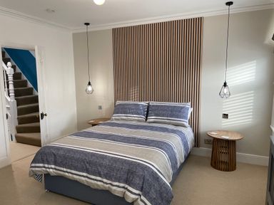 A bedroom with a striped bedspread two pendant lights and wooden side tables at Happy Place in Sheringham