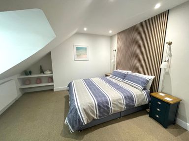 A bedroom with a double bed striped bedding a wood slat headboard two bedside tables and wall sconces at Happy Place in Sheringham