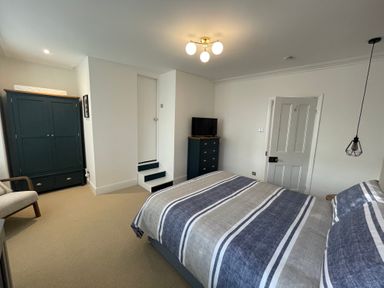 A bedroom with a bed striped bedding a wardrobe a chair a chest of drawers and a door at Happy Place in Sheringham