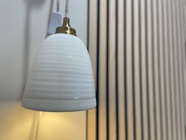 A white hanging lamp with brass fixtures near a wall with vertical wooden slats at Happy Place in Sheringham