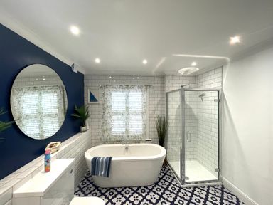 A bathroom with a bathtub shower toilet round mirror and patterned floor at Happy Place in Sheringham