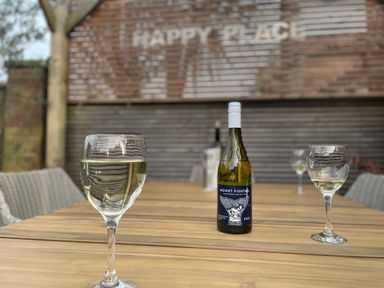 A wooden table with a bottle of Mount Fishtail white wine and two wine glasses at Happy Place in Sheringham
