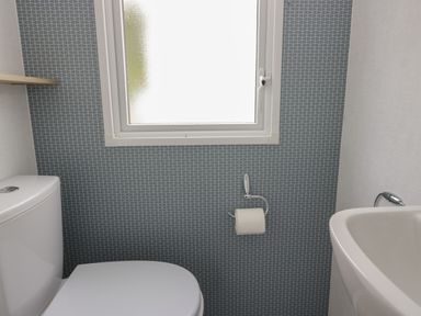 A bathroom with a toilet paper holder toilet and sink under a window at Oak in Denny