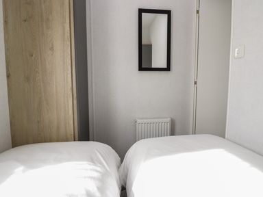 A bedroom with two single beds a wooden wardrobe a wall mirror and a radiator at Oak in Denny