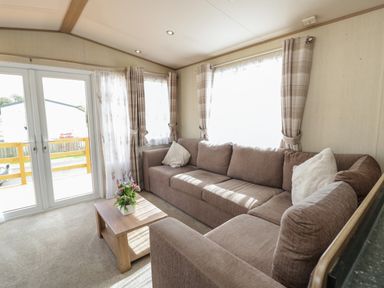 A living room with a brown sectional sofa, a wooden coffee table with flowers, plaid curtains, and glass doors at Hazel in Denny