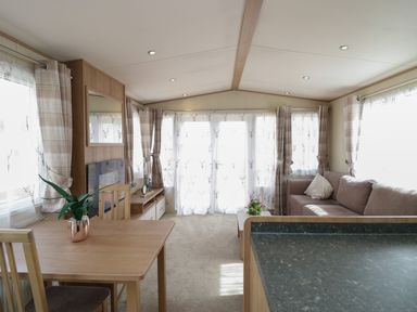 A living room with a sofa, a wooden dining table, a television, curtains, and a coffee table with flowers at Hazel in Denny