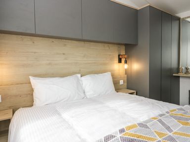 A bedroom with a double bed white pillows gray and yellow blanket wooden headboard and gray cabinets at Hazel in Denny