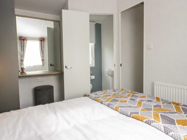 A bedroom with a bed a patterned blanket a dressing table with a mirror and an open door to a bathroom at Hazel in Denny