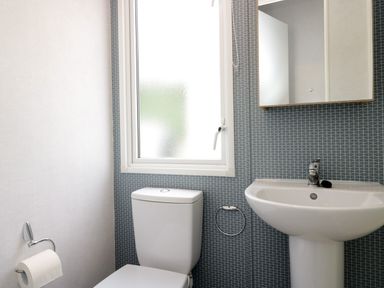 A bathroom with a toilet a sink a mirror a window and a toilet paper holder at Hazel in Denny
