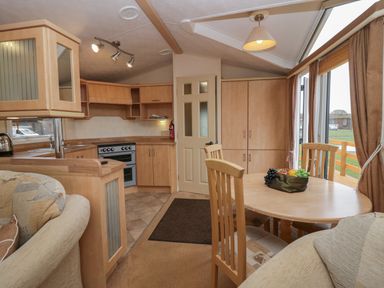 A kitchen with wooden cabinets and a dining table with chairs and fruit bowl at Birch in Denny
