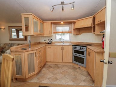 A kitchen with wooden cabinets a double oven a sink a kettle and a window with blinds at Birch in Denny