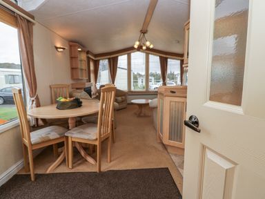 A dining area with a wooden table and four chairs next to a living room with sofas and a coffee table at Birch in Denny