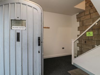 An entrance hall with a closed door labeled Tomlinsons Apartments a coat rack on the wall and stairs with glass panels and stone wall at The Coquet Nest in Rothbury