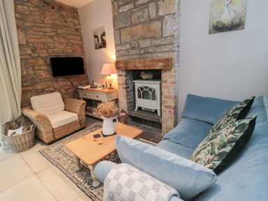 A living room with a blue sofa with patterned cushions a wicker armchair a wooden coffee table and a stone fireplace at The Coquet Nest in Rothbury
