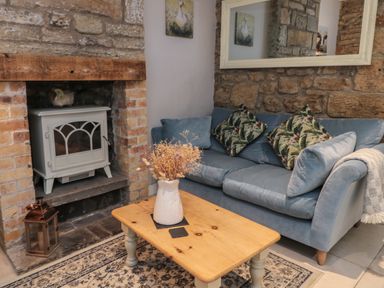 A living room with a blue sofa a wooden coffee table with a vase and fireplace at The Coquet Nest in Rothbury
