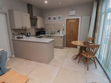 A kitchen with beige cabinets and white countertop next to a wooden table with two chairs by a window at The Coquet Nest in Rothbury
