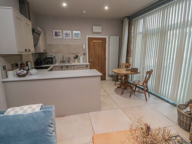 A kitchen and dining area with wooden chairs and round table near large vertical blinds at The Coquet Nest in Rothbury