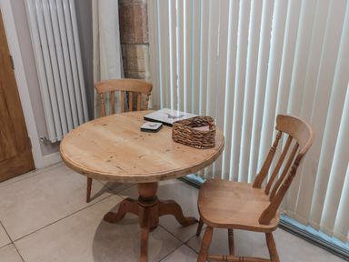 A wooden round table with two wooden chairs near vertical blinds and a radiator at The Coquet Nest in Rothbury