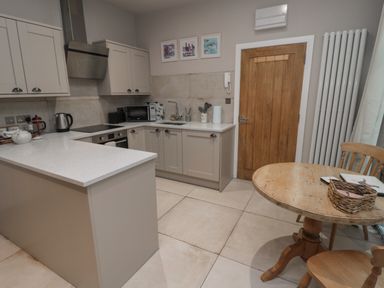 A kitchen with white cabinets and appliances next to a wooden table and chairs at The Coquet Nest in Rothbury