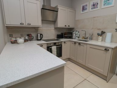 A kitchen with beige cabinets white countertops and appliances including a kettle microwave and oven at The Coquet Nest in Rothbury
