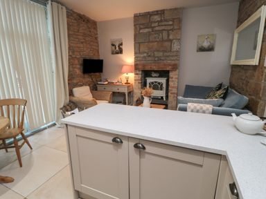 A living area with chairs a sofa a stone fireplace a desk with a lamp and a kitchen island at The Coquet Nest in Rothbury
