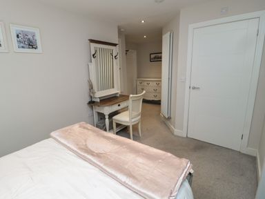 A bedroom with a bed a white dressing table with a mirror and chair and a white chest of drawers at The Coquet Nest in Rothbury