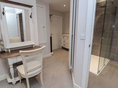 A room with a white vanity table and chair next to a walk in shower and a chest of drawers at The Coquet Nest in Rothbury