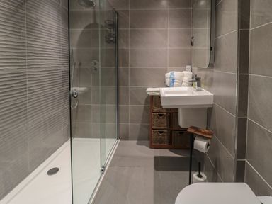 A bathroom with a walk in shower sink with towels and storage baskets at The Coquet Nest in Rothbury