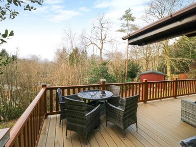 An outdoor deck with a round glass table and four wicker chairs surrounded by trees at Esk Pike 9 Skiptory Howe White Cross Bay near Windermere