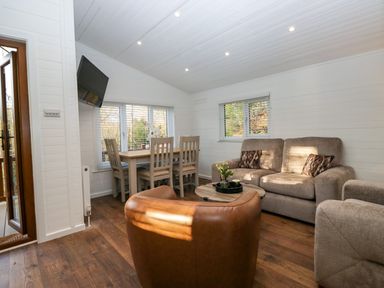 A living room with a dining table and chairs a sofa an armchair a round coffee table and a mounted television at Esk Pike 9 Skiptory Howe White Cross Bay near Windermere