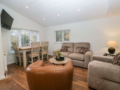 A living room with a dining table and chairs a sofa an armchair a round coffee table and a wall-mounted TV at Esk Pike 9 Skiptory Howe White Cross Bay near Windermere