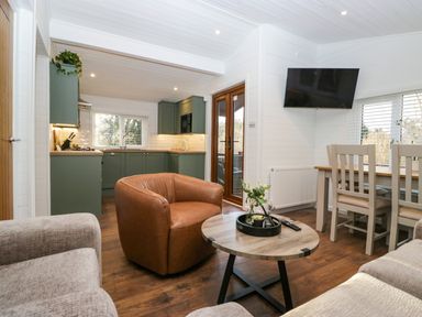 A living room with a brown leather chair a wooden coffee table and a dining table near kitchen cabinets at Esk Pike 9 Skiptory Howe White Cross Bay near Windermere