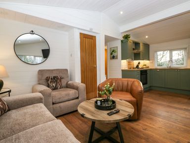 A living room with armchairs a round wooden coffee table and a kitchen with green cabinets at Esk Pike 9 Skiptory Howe White Cross Bay near Windermere