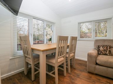 A dining area with a wooden table and four chairs next to windows and a beige sofa in a white room at Esk Pike 9 Skiptory Howe White Cross Bay near Windermere