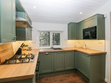 A kitchen with green cabinets wooden countertops a gas stove a microwave a sink and a window with blinds at Esk Pike 9 Skiptory Howe White Cross Bay near Windermere