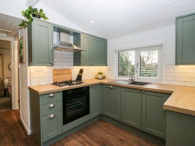 A kitchen with green cabinets wooden countertops a gas stove oven a sink under a window and white tiled walls at Esk Pike 9 Skiptory Howe White Cross Bay near Windermere