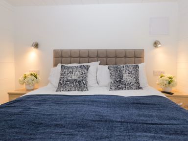 A bed with textured headboard two patterned pillows two bedside tables with flowers and wall lights at Esk Pike 9 Skiptory Howe White Cross Bay near Windermere