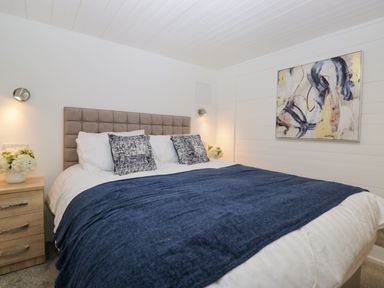 A bedroom with a bed covered in white and blue bedding two pillows a wooden bedside table with flowers and an abstract painting on the wall at Esk Pike 9 Skiptory Howe White Cross Bay near Windermere