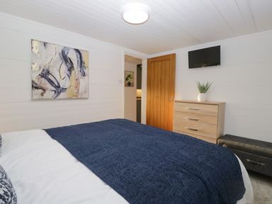 A bedroom with a bed covered by a blue blanket a wooden dresser with a plant and a wall-mounted television at Esk Pike 9 Skiptory Howe White Cross Bay near Windermere