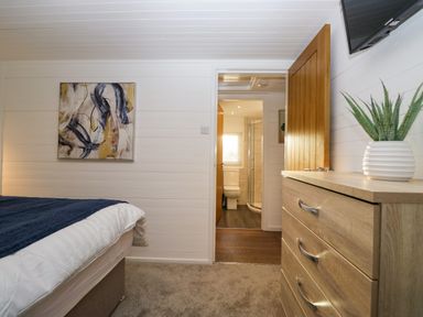 A bedroom with a bed a wooden dresser a plant, an open door leading to a bathroom with a toilet and shower at Esk Pike 9 Skiptory Howe, White Cross Bay near Windermere