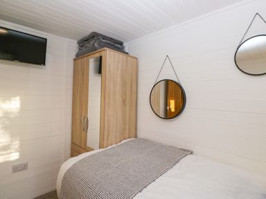 A bedroom with a bed a wooden wardrobe with mirrors and two round mirrors on the wall at Esk Pike 9 Skiptory Howe White Cross Bay near Windermere