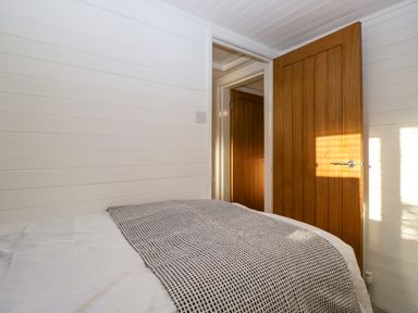 A bedroom with a bed covered by a patterned blanket wooden doors and white paneled walls at Esk Pike 9 Skiptory Howe White Cross Bay near Windermere